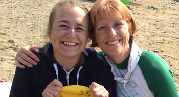 Two women smiling to the camera. One has their arm around the other.