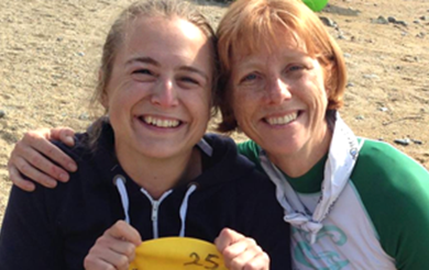 Two women smiling to the camera. One has their arm around the other.
