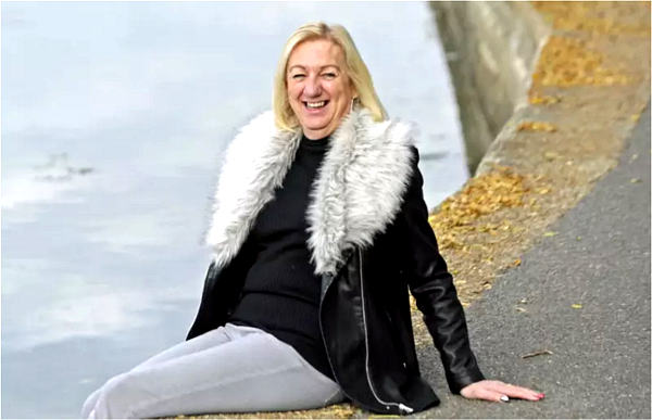 Tina Young sits at the waterside, smiling at the camera.