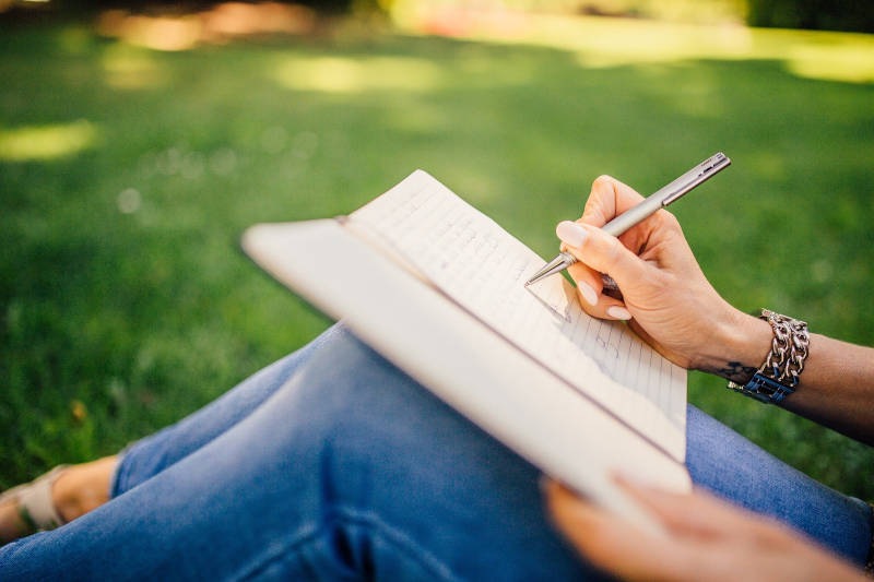 A woman sits on grass and writes in her notebook